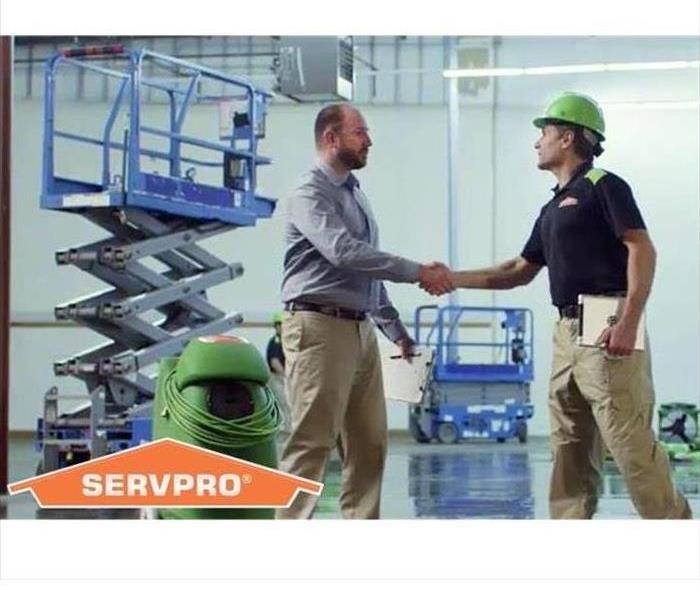 SERVPRO technician shaking hands with a customer in a warehouse with equipment in it.