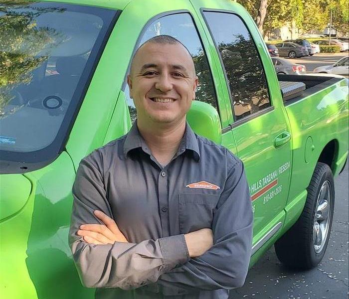 SERVPRO technician smiling and leaning against a green truck